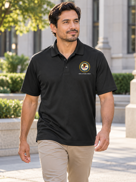 Black men's Dri Fit polo with source DOJ seal and exact Office of Public Affairs caption outdoors at a civic office