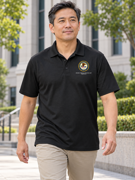 Black ATF men's Dri Fit polo with its exact source DOJ seal and Alcohol, Tobacco, Firearms and / Explosives caption at a federal office exterior