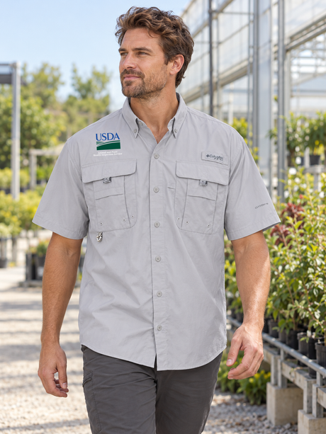 APHIS men's Columbia Bahama II Cool Grey shirt at a greenhouse inspection-program setting; exact own source USDA and Animal and Plant Health Inspection Service artwork.