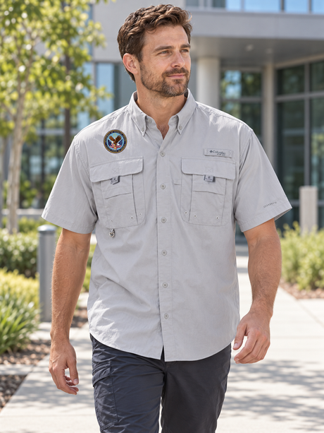VA Men's Columbia Bahama II Cool Grey shirt with original Department of Veterans Affairs seal outside a veterans services administration office.