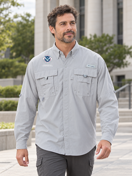ICE men's Cool Grey Columbia Bahama II long-sleeve shirt on a coordinator walking outside an urban federal office campus.
