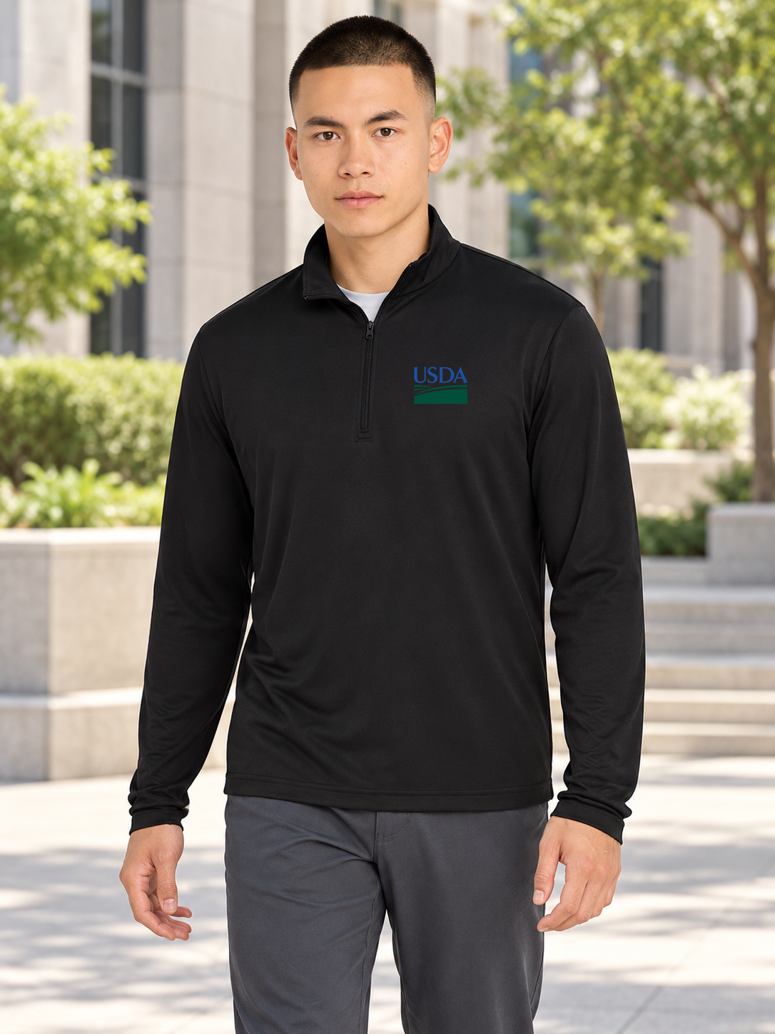 USDA black men's long-sleeve quarter-zip with the original blue and green USDA artwork on the wearer's left chest, shown outdoors in the approved office courtyard scene.