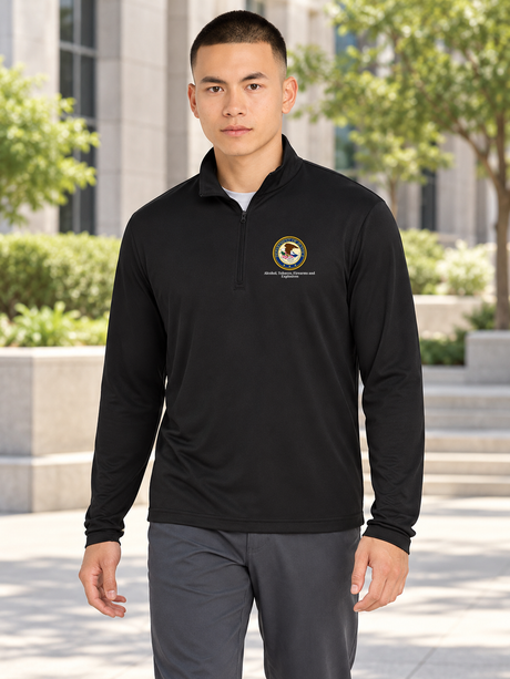 Black men's lightweight quarter-zip with its original Department of Justice seal and Alcohol, Tobacco, Firearms and Explosives caption, shown in the approved outdoor office scene.